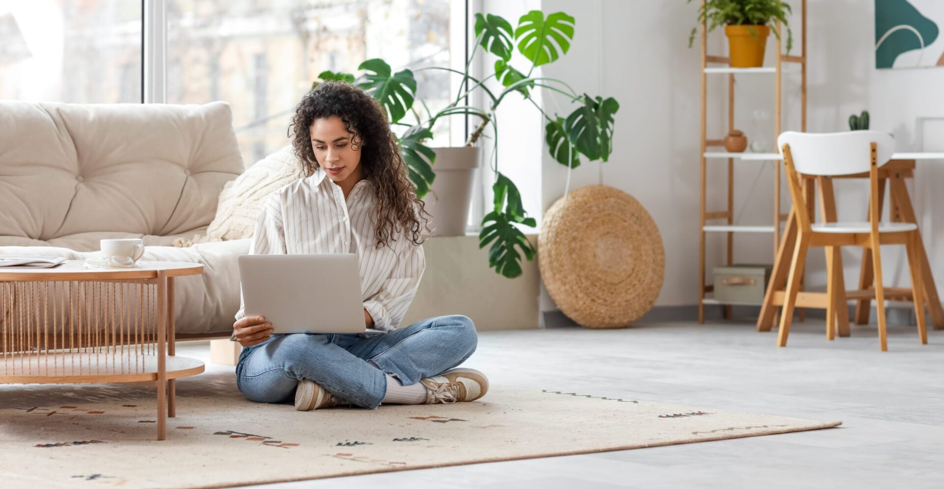 young woman sitting on the floor of her living room on her laptop